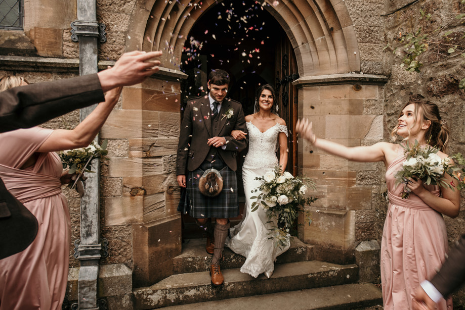 groom and bride walking out of church doorway with bridesmaids throwing confetti